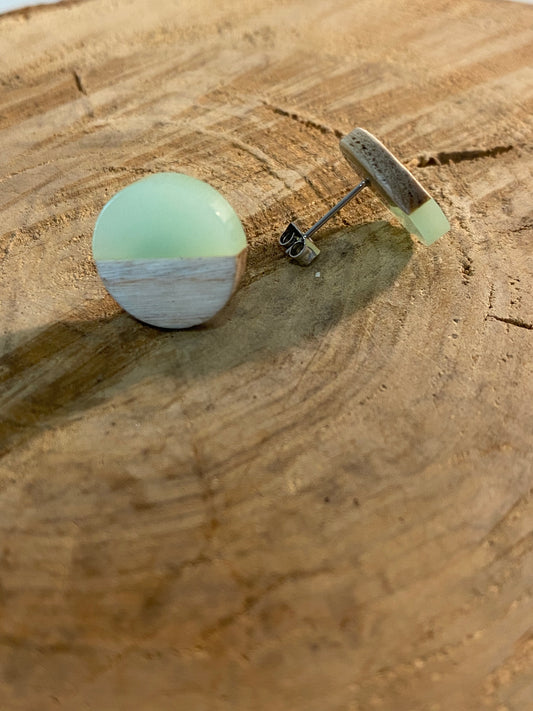 Ein Paar runde Holzohrstecker mit Halbmond-Design aus blassgrünem Harz und hellem Holz ruhen elegant auf einer strukturierten Holzoberfläche.