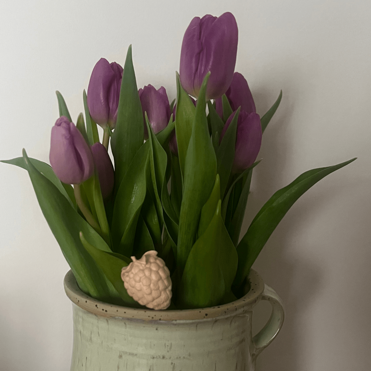 Holzfigur in Himbeerform an einem Blumentopf mit violetten Tulpen.