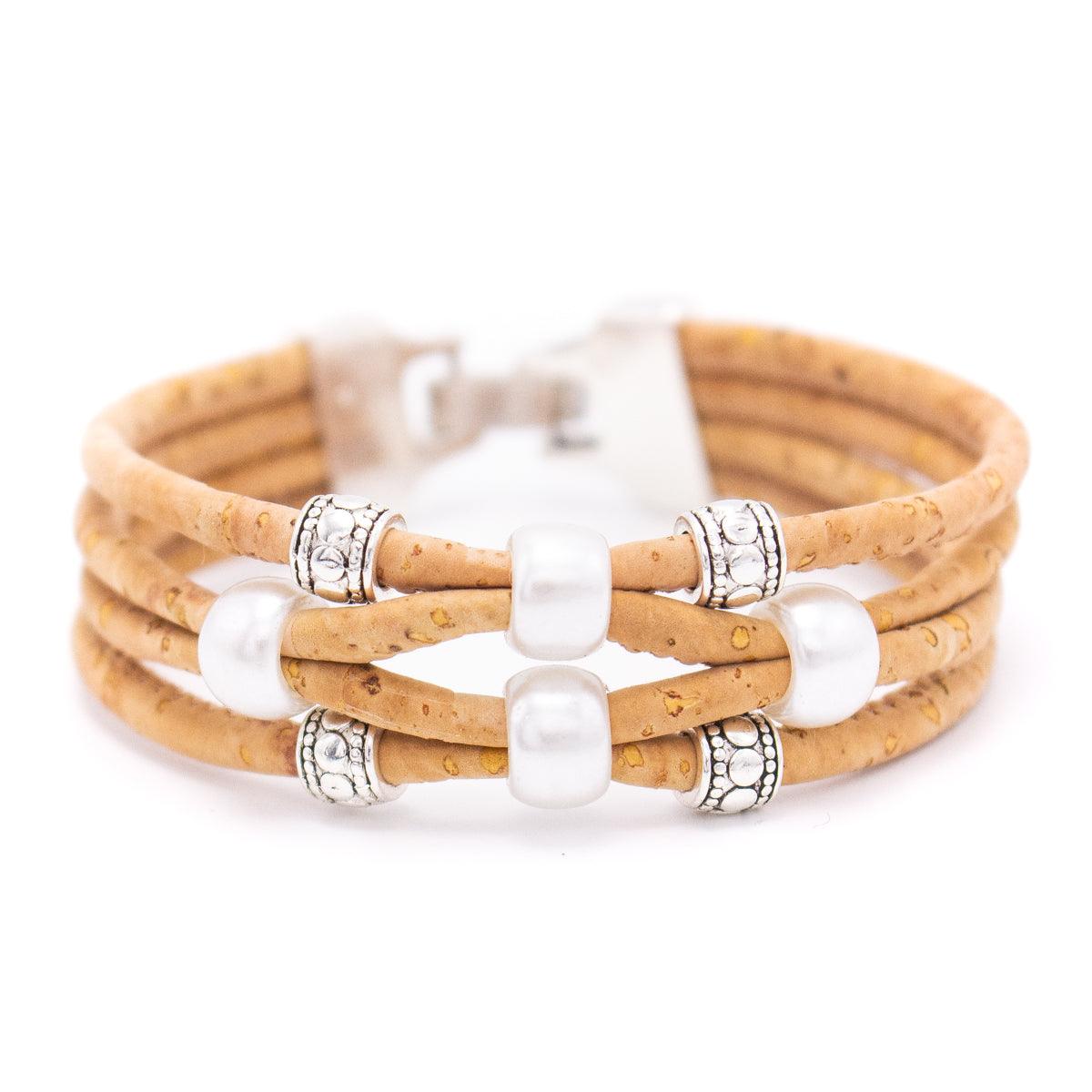 Ein hellbraunes, umweltfreundliches Korkarmband mit drei Strängen, die mit silbernen und weißen perlenähnlichen Perlen verziert sind und mit einem nickelfreien Verschluss aus Edelstahl geschlossen werden.