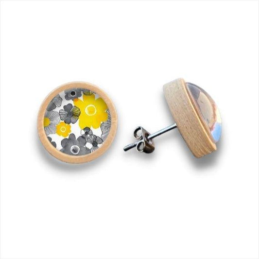 Ein Paar runde Ohrstecker aus Holz mit einer Umrandung aus Birkenholz, die ein leuchtendes gelbes, schwarzes und weißes Blumenmuster unter einer klaren Cabochonglaslinse zeigen. Ein Ohrring ist von vorne und der andere im Profil abgebildet.
