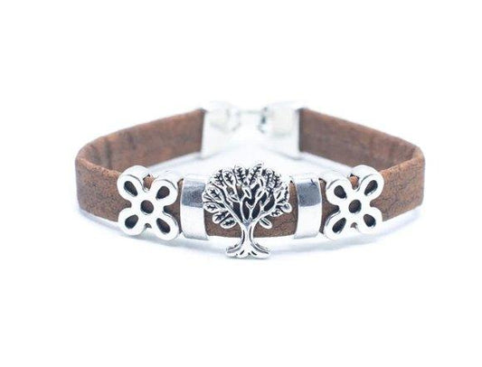 Ein braunes Wildlederarmband von Wood Stud mit einem zentralen silbernen Lebensbaum-Charm mit zwei silbernen Blumenakzenten, gefertigt aus umweltfreundlichen Materialien und vor einem weißen Hintergrund.