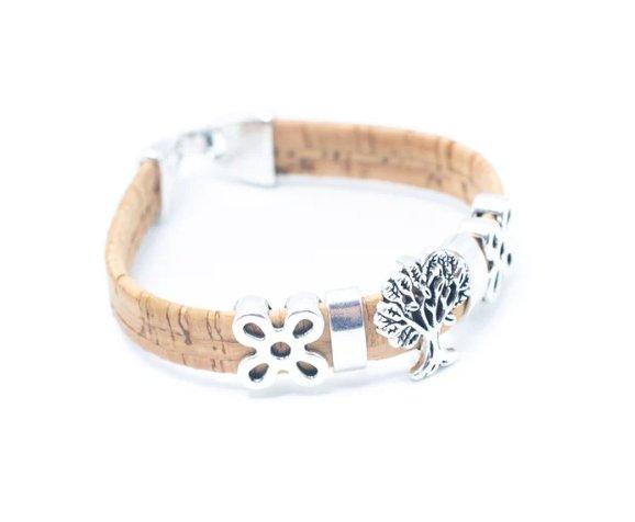 Ein handgefertigtes Kork-Armband von wood stud mit silbernen, nickelfreien Edelstahl-Charms wie Blume und Baum, umweltfreundlich auf weißem Hintergrund präsentiert.
