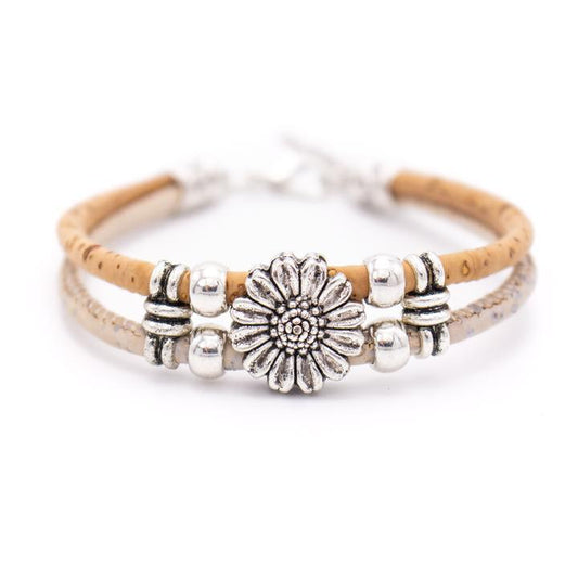 Ein doppelreihiges, umweltfreundliches, hellbraunes Kork-Armbändchen aus Holz mit einem silbernen Gänseblümchen-Anhänger in der Mitte und nickelfreien Edelstahlperlen als Akzente.