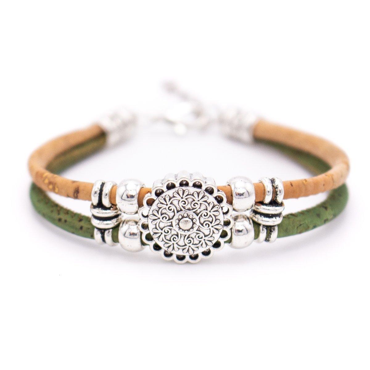 Ein Holzarmband mit hellbraunen und grünen Kordeln, silbernen Perlen und einem runden, floralen Mittelstück aus Silber. Hergestellt aus umweltfreundlichen Korkbändern und nickelfreiem Edelstahl - ideal für empfindliche Haut.