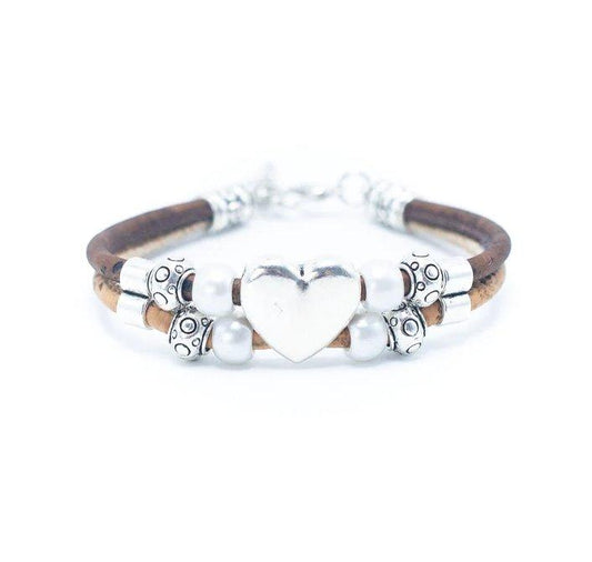 Das braune, vegane Kork-Armband mit Holznieten zeigt in der Mitte ein großes silbernes Herz, das zwischen kunstvoll gemusterten Silberperlen und perlenartigen Akzenten auf weißem Hintergrund liegt.