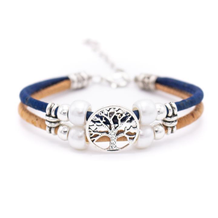 Ein Kork-Armbänder mit Holzstiften, blauen und hellbraunen Bändern, silbernen Akzenten, weißen Perlen und einem zentralen Lebensbaum-Anhänger aus nickelfreiem Edelstahl wird auf einem weißen Hintergrund gezeigt.