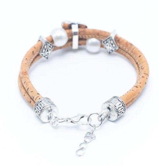 Das Holzstollenarmband besteht aus zwei hellbraunen Kork-Armbändern mit silberfarbenen, nickelfreien Edelstahlperlen und weißen, runden Akzenten und ist mit einem Metallverschluss und einer verstellbaren Kette versehen.