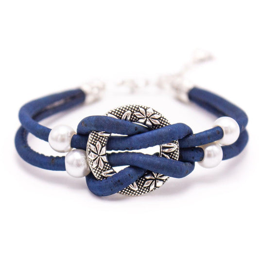 Ein blaues Kordel-Kork-Armband von wood stud mit einem zentralen, verschnörkelten, silberfarbenen, runden Anhänger mit floralen Mustern und vier weißen Perlen, gefertigt aus nickelfreiem Edelstahl für nachhaltige Mode.