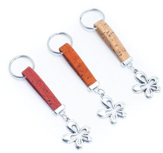Drei nachhaltige Kork-Schlüsselanhänger aus Holz mit silbernen Blumenanhängern, jeweils mit einem rechteckigen Korkband in Rot, Orange und Naturbraun, sind als vegane Alternative nebeneinander auf weißem Grund angeordnet.