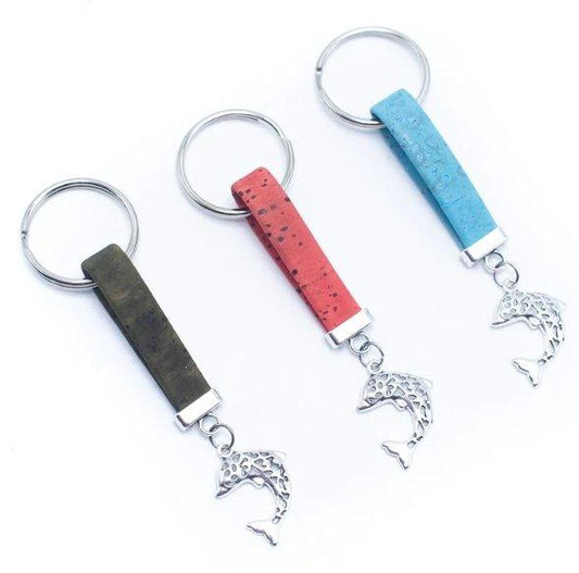 Drei umweltfreundliche Kork-Schlüsselanhänger von wood stud, mit einem Delfin-förmigen Metallanhänger und grünen, roten und blauen Streifen, sind an silbernen Schlüsselringen nebeneinander auf weißem Hintergrund angeordnet.