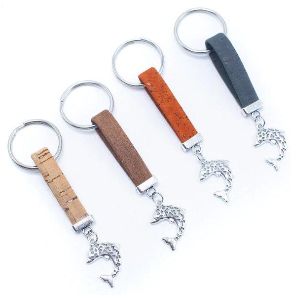 Set aus vier Kork-Schlüsselanhängern aus Holz, jeder mit einem silbernen Anhänger in Form eines Delphins. Die Metallringe und flachen Korkriemen in Beige, Braun, Orange und Dunkelgrau verleihen eine nachhaltige Note.