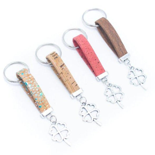 Vier hölzerne Kork-Schlüsselanhänger mit silbernen vierblättrigen Kleeanhängern. Jeder umweltfreundliche Schlüsselanhänger verfügt über eine einzigartige Schleife: hellbraun mit blauen Flecken, Naturkork, rosa Kork oder brauner Kork - alle mit silbernen Schlüsselringen.