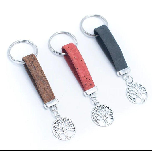 Drei Schlüsselanhänger aus Holz mit Metallringen und Lebensbaum-Anhängern, jeweils mit einem Band aus nachhaltigem Kork in Braun, Rot und Schwarz - eine attraktive vegane Option - nebeneinander auf weißem Hintergrund.