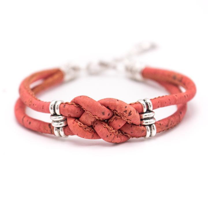 Ein korallenfarbenes Kork-Armbändchen mit einem zentralen Knoten und silbernen, nickelfreien Edelstahlringen auf weißem Grund.