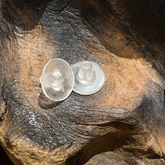 Zwei klare Kunststoff-Ohrsteckerverschlüsse aus Holzstollen ruhen auf einer strukturierten, braunen Holzoberfläche mit sichtbarer Maserung und Rillen.