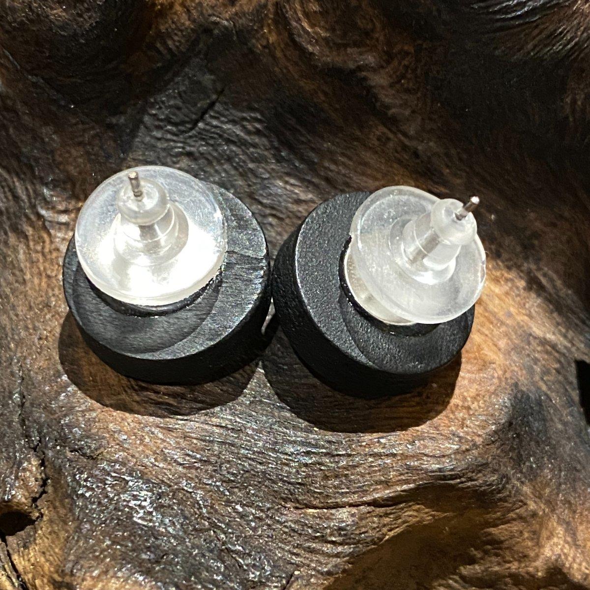 Nahaufnahme von zwei runden Ohrsteckerverschlüssen aus schwarzem und klarem Kunststoff, die auf einer strukturierten braunen Holzoberfläche ruhen.