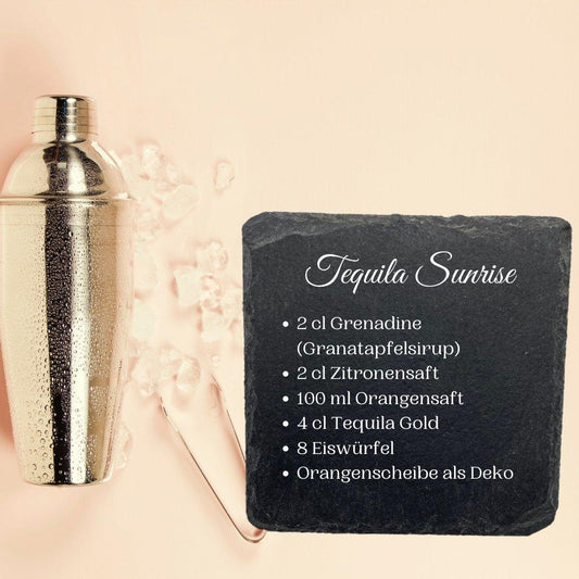 Ein Cocktailshaker aus Metall steht neben Eiswürfeln auf einer hellen Fläche. Daneben zeigt ein schwarzer Holzständer Naturschiefer-Schieferuntersetzer ein Tequila-Sunrise-Rezept auf Deutsch, das Grenadine, Tequila und eine Orangenscheibe als Zutaten aufführt.