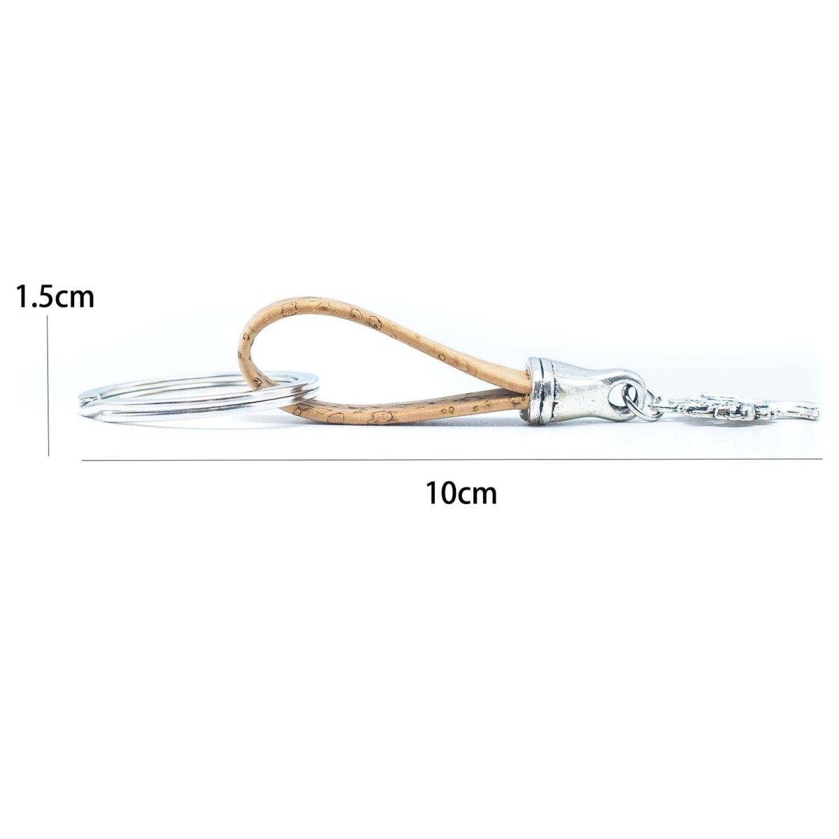 Dieser Kork-Schlüsselanhänger mit Holznieten verfügt über ein geschlungenes hellbraunes Lederband, eine silberne Schließe und einen Schlüsselring, misst 10 x 1,5 cm und ist umweltfreundlich. Abgebildet auf einem weißen Hintergrund mit Messlinien.