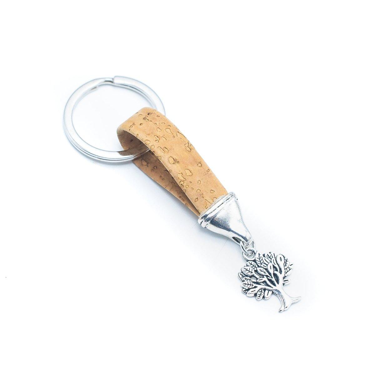 Der Holzstollen Kork-Schlüsselanhänger kombiniert eine hellbraune Korkschlaufe mit silbernem Baum-Anhänger an einem runden Schlüsselring - stilvoll und nachhaltig, das perfekte Accessoire.
