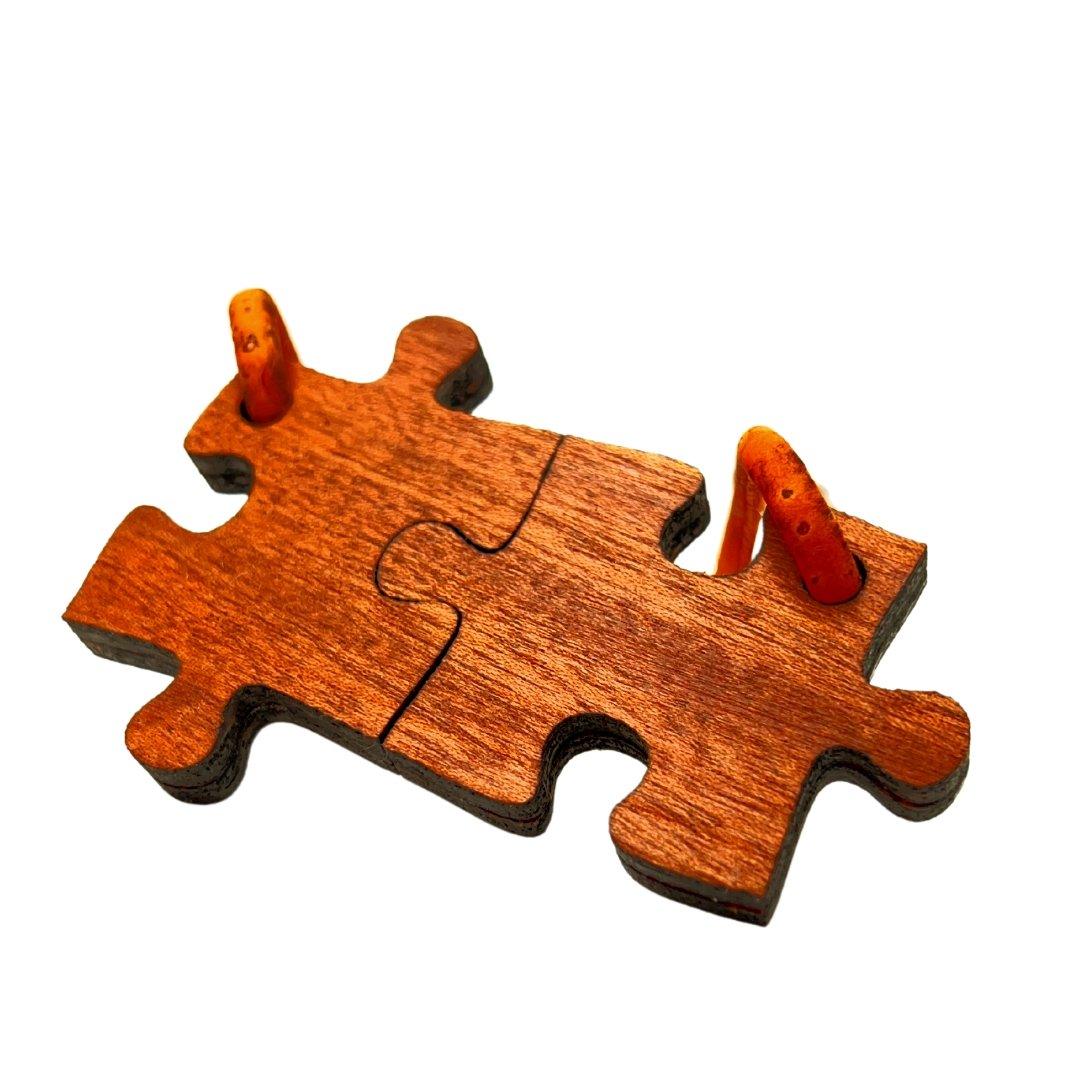 Zwei Holzpuzzleteile mit natürlicher Maserung sind miteinander verbunden und zeigen jeweils eine kleine orangefarbene Karotte, die aus einem Loch hervorlugt, vor einem weißen Hintergrund.