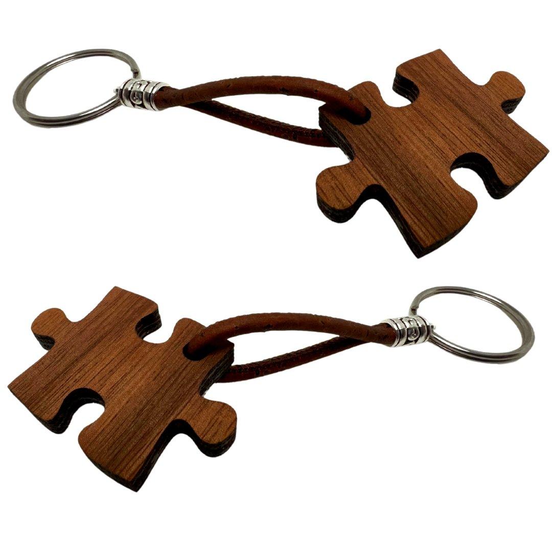 Zwei Holz-Schlüsselanhänger von wood stud mit natürlicher Maserung sind als Puzzleteile gestaltet und durch braune Lederloops an Metallringen befestigt - ein schönes Beispiel nachhaltigen Designs.