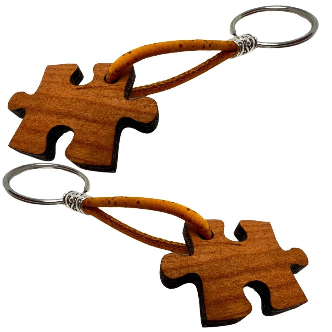 Zwei Holz-Schlüsselanhänger von wood stud in Puzzleform, jeweils mit Metallring und braunem Band. Die natürliche Holzmaserung unterstreicht das nachhaltige Design auf weißem Hintergrund.