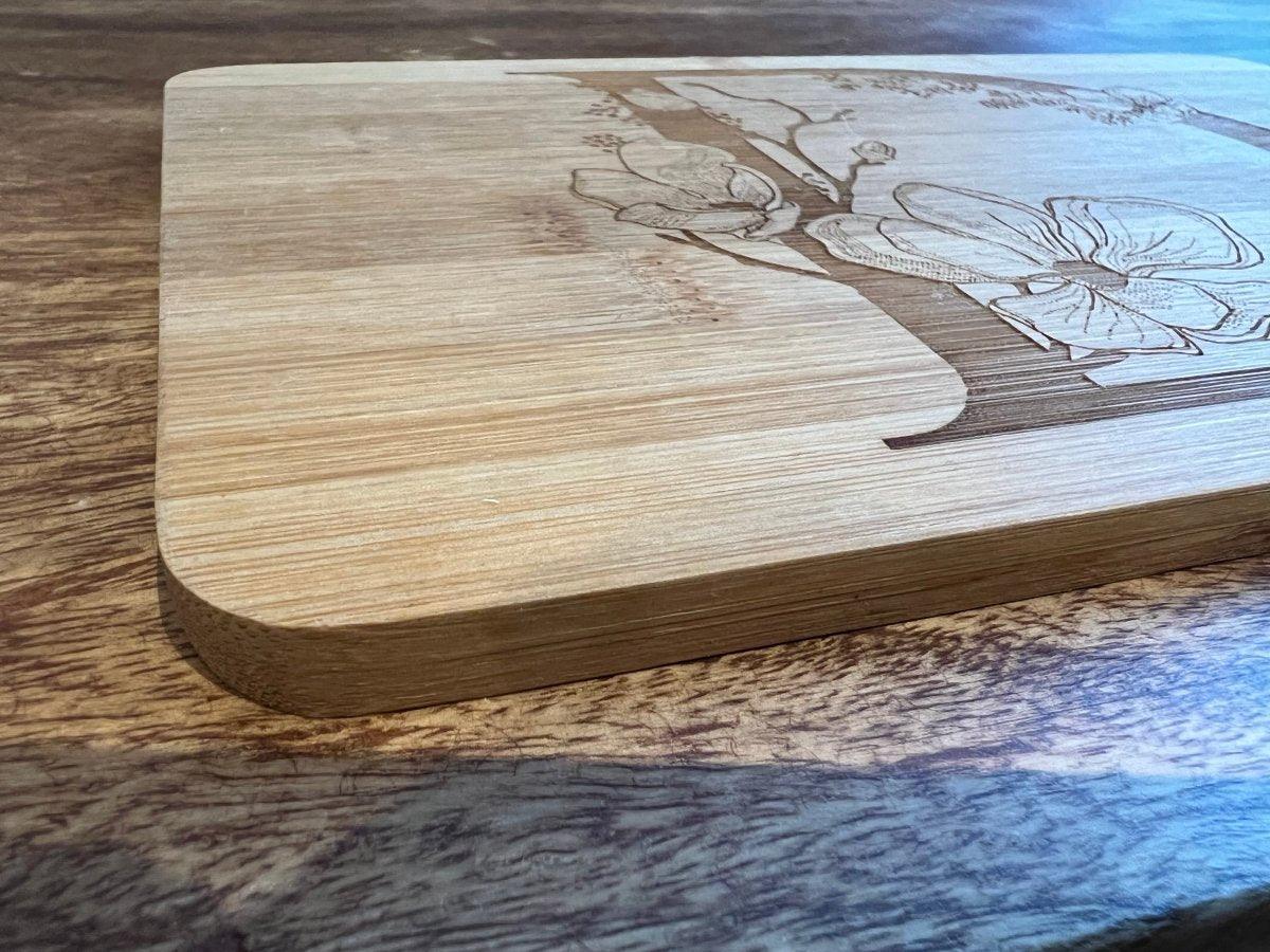 Eine Nahaufnahme eines Schneidebretts mit abgerundeten Kanten, das eine elegante florale Holzgravur aufweist und auf einer Holzoberfläche ruht - eine perfekte Geschenkidee für jede Küche.