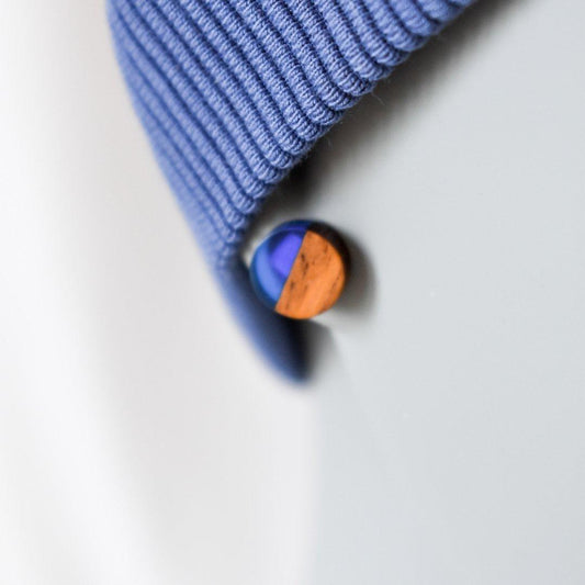 Eine Nahaufnahme eines runden Holzohrsteckers mit blauem und hölzernem Muster, der an einem Ohr getragen wird. Die Person trägt auch ein geripptes Twister Stirnband, das das Ohr leicht bedeckt. Der Hintergrund erscheint unscharf.
