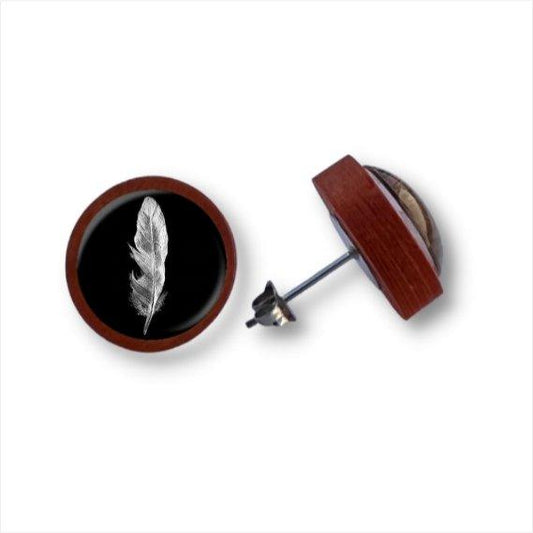 Ein Paar runder Holzohrstecker mit Birkenholzkanten und einem schwarzen Zentrum mit einer detaillierten weißen Feder unter einer Cabochon-Glaslinse. Ein Ohrring zeigt nach oben, der andere liegt auf der Seite und zeigt die Rückseite.