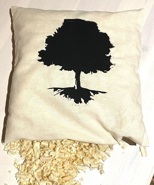Ein beiges Holzstollen-Zirbenkissen mit schwarzer Baumsilhouette ruht auf einer hellen Fläche, aus einer Ecke quillt duftende Zirbenspäne - perfekt, um Schlafstörungen auf natürliche Weise zu lindern.